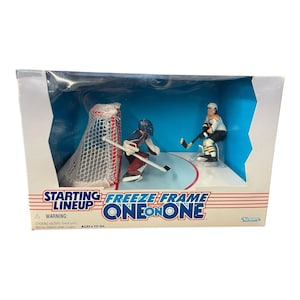 May include: A boxed "Starting Lineup Freeze Frame One on One" hockey figurine set. The set includes two hockey players, a net, and a hockey rink base. The box has the text "Starting Lineup Freeze Frame One on One" and a warning about small parts.