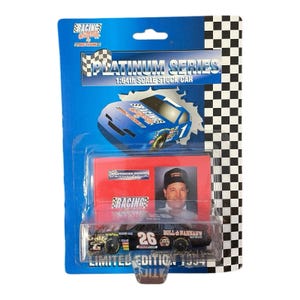 Op de afbeelding: Een zwart en goudkleurig stock car op schaal 1:64, met het nummer "26", in een blauw-witte verpakking. De verpakking vermeldt "Platinum Series" en "Limited Edition 1994". De verpakking bevat ook een foto van een man met een hoed.