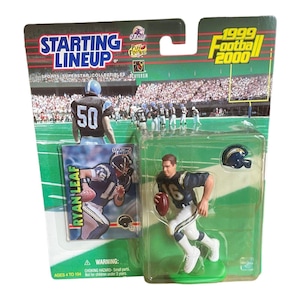 May include: A Starting Lineup 1999 Football 2000 action figure of Ryan Leaf in a Chargers uniform. The figure is in a clear plastic case with a football card and a miniature helmet. The packaging features a football field background.