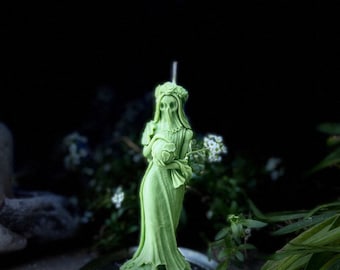 Può includere: Una candela verde scolpita a forma di donna con un velo e che tiene un mazzo di fiori. La candela è appoggiata su un vassoio d'argento con un disegno di pentagramma.