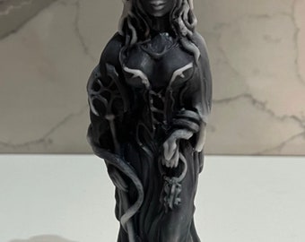 May include: A black and white candle sculpture of a woman with long hair and a snake wrapped around her arm. She is holding a key in her hand. The candle is decorated with intricate details and has a white key on top.