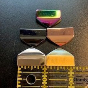 May include: Five iridescent glass tiles in various colors, including black, brown, gold, silver, and green, arranged in a row on a ruler. The tiles are approximately 1 inch wide and 1/2 inch tall.
