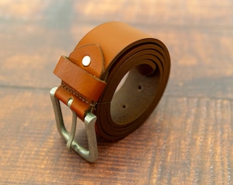 May include: A brown leather belt with a silver buckle. The belt is rolled up and the buckle is facing the camera.