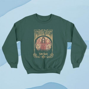 May include: A dark green sweatshirt with a vintage-style graphic of a woman in a red dress standing in a field. The graphic includes the text "Wuthering Heights" and "Kate Bush".