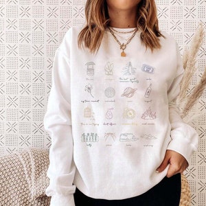 May include: White sweatshirt with a colorful graphic print of various icons and text. The text includes "my time spent", "the last great american dynasty", "wine", "shelf life", "good woman", "home", "epiphany", and more.