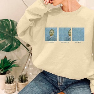 Puede incluir: Una sudadera de color beige claro con cuello redondo y mangas largas. La sudadera presenta tres imágenes de Vincent van Gogh, cada una con el texto "Van Gogh" debajo.