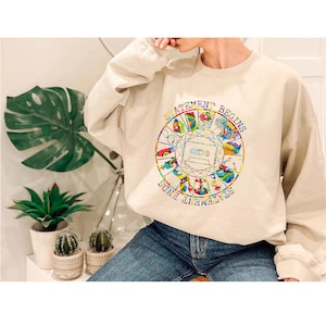 Könnte beinhalten: Beiges Sweatshirt mit farbenfrohem Grafikdesign. Das Design zeigt einen Kreis mit einer Kassette in der Mitte und den Worten "STATEMENT BEGINS" und "STATEMENT ENDS" am Rand. Das Sweatshirt wird mit einer blauen Jeans kombiniert.