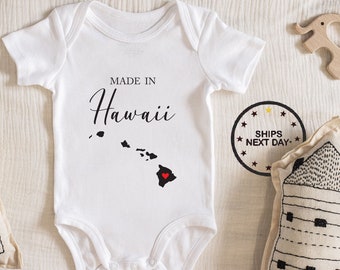 May include: White baby onesie with black text that reads "Made in Hawaii" and a black outline of the Hawaiian islands with a red heart in the center of the largest island.