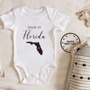 May include: White baby onesie with the text "Made in Florida" and an outline of the state of Florida with a red heart in the center.