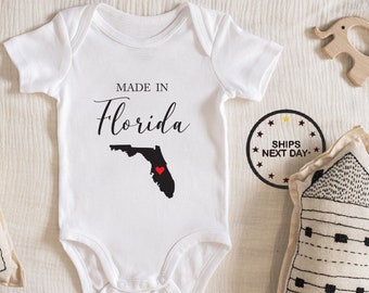 May include: White baby onesie with the text "Made in Florida" and an outline of the state of Florida with a red heart in the center.