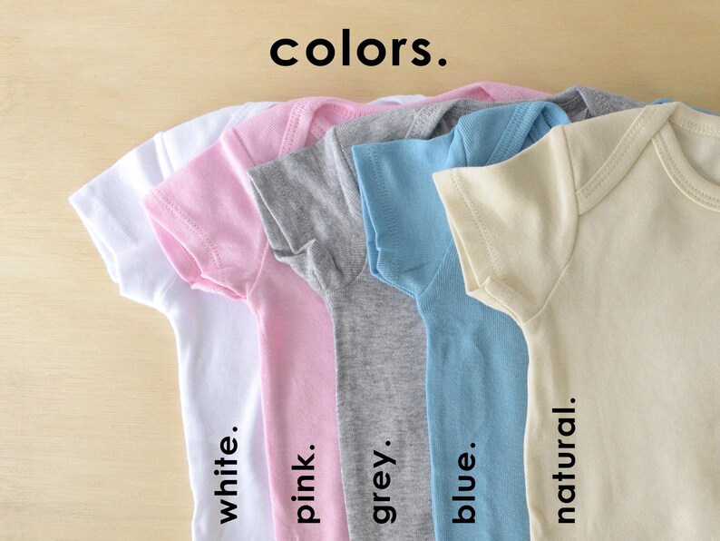 May include: Five baby onesies in different colors: white, pink, grey, blue, and natural. The onesies are laid out in a row, with the white onesie on the left and the natural onesie on the right. The text "colors." is written above the onesies.