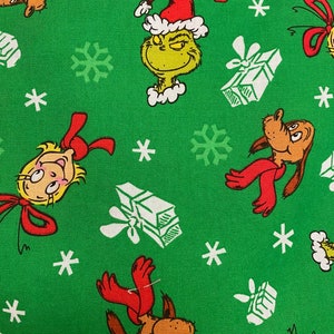 Może przedstawiać: Zielony materiał z powtarzającym się wzorem Grincha, psa Maxa, Cindy Lou Who, płatk&oacute;w śniegu i prezent&oacute;w. Grinch ma na sobie czapkę Świętego Mikołaja i ma złośliwy uśmiech. Pies Max ma na sobie czerwony szalik. Cindy Lou Who ma na sobie czerwoną kokardkę. Prezenty są białe z czerwoną kokardką.