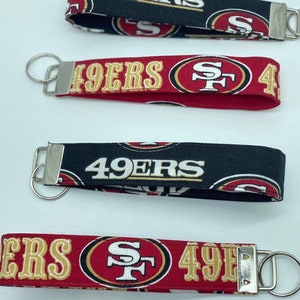 May include: Four different keychains featuring the San Francisco 49ers logo. The keychains are red, black and gold with the team's logo and the words "49ers" printed on them.