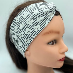 May include: A white and black patterned headband with a design of cartoon teeth. The headband is made of a soft, stretchy fabric and is designed to be worn as a turban.
