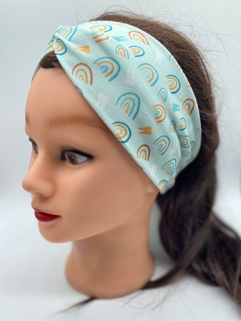 May include: A light blue headband with a pattern of colorful rainbows and white teeth. The headband is made of a soft, stretchy fabric and is perfect for keeping hair out of your face.