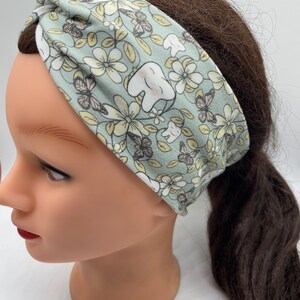 May include: A light green headband with a floral and tooth pattern. The headband is made of a soft, stretchy fabric and is perfect for keeping hair out of your face.