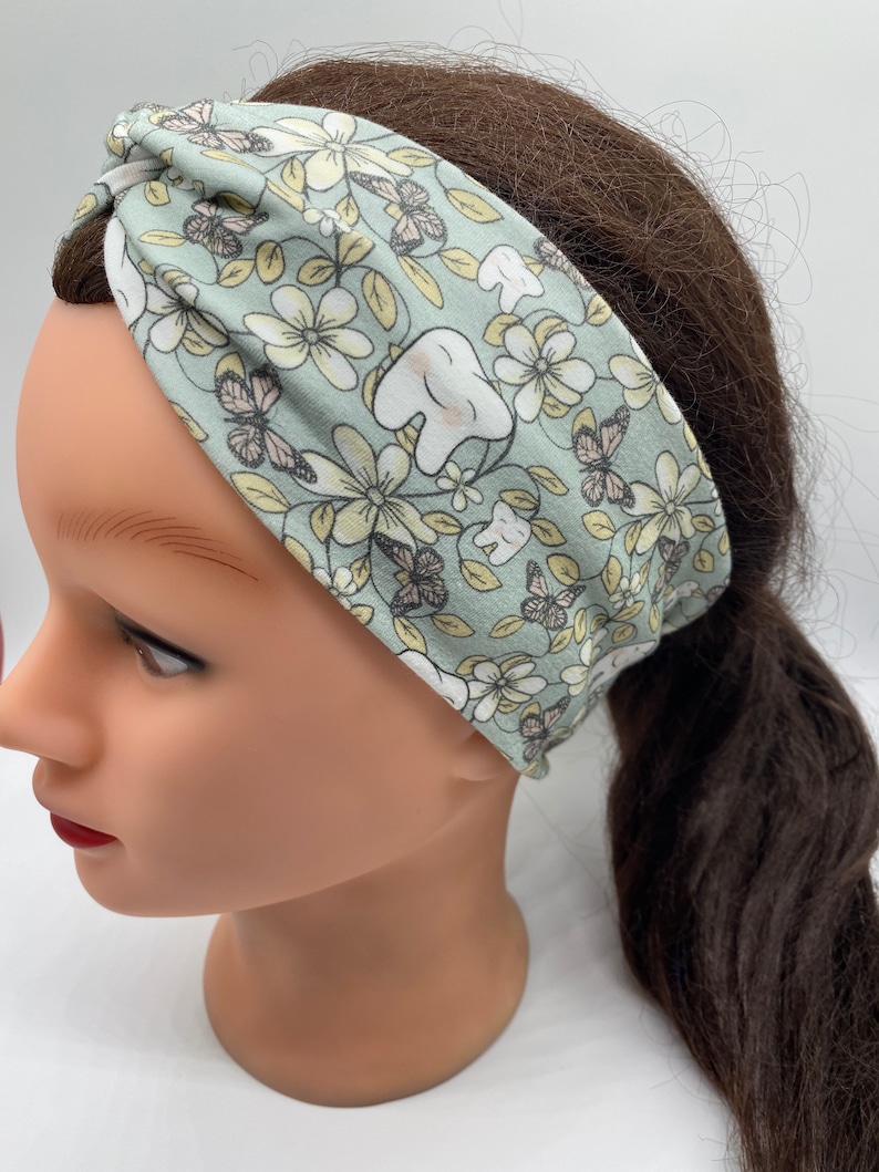 May include: A light green headband with a floral and tooth pattern. The headband is made of a soft, stretchy fabric and is perfect for keeping hair out of your face.