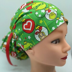 Może przedstawiać: Zielony chirurgiczny czepek z motywem świątecznym z Grinchem, Cindy Lou Who i ozdobami. Czepek ma czerwony krawat.