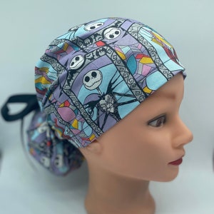 May include: A blue, purple, pink and yellow patterned surgical scrub hat with a black tie. The pattern features a stained glass design with images of Jack Skellington from The Nightmare Before Christmas.