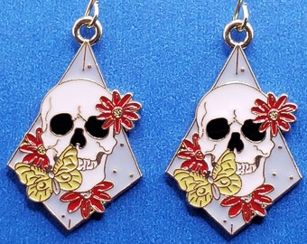 May include: A pair of silver earrings with a white skull and red and yellow flowers on a diamond-shaped base.