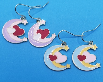 May include: A pair of silver earrings with a crescent moon design. Each earring features a pink and white heart with a red center, and a gold star. The earrings are on a blue background.