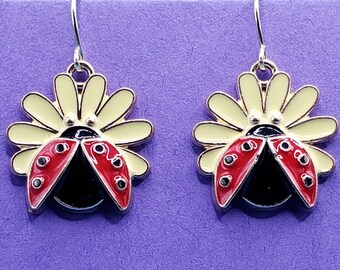 May include: A pair of dangle earrings featuring a red and black ladybug with yellow wings on a yellow daisy flower.