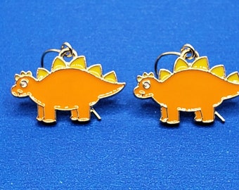 May include: A pair of orange dinosaur earrings with yellow spines. The earrings are made of metal and have a hook closure.