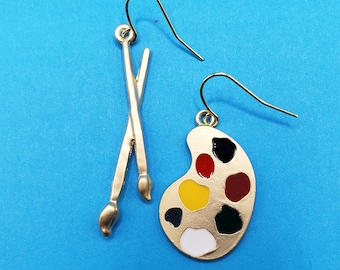 May include: Gold-tone earrings with a paint palette and paintbrushes. The palette has six paint wells in red, yellow, white, black, and two shades of brown.