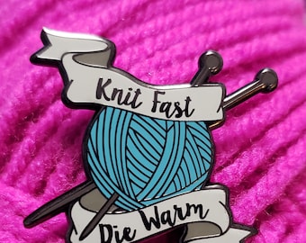 May include: A silver enamel pin with a blue yarn ball, two knitting needles, and a banner that reads "Knit Fast Die Warm".