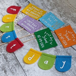 May include: A colorful felt banner with the words "First day of school" and the date "02-09-2024". The banner is made up of individual flags with the letters "First day" and the date on separate flags. The flags are attached to wooden sticks.