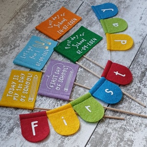 May include: A colorful felt banner with the words "First Day of School" and the dates "02-09-2024" and "24-07-2024". The banner is decorated with pencils and other school-themed imagery.