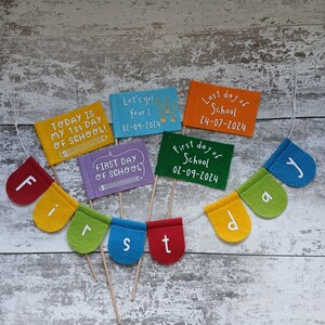 May include: A felt banner with the word "first" spelled out in colorful felt letters. There are also five small felt flags with messages about the first and last day of school, including dates.