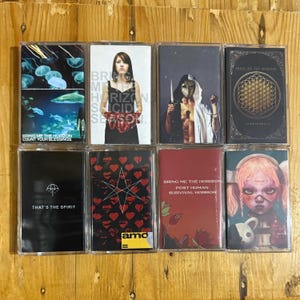 以下が含まれることがあります： Bring Me The Horizonのアルバムアートワークが描かれた8つのカセットテープ。水中シーン、ポートレート、幾何学模様など、デザインは様々です。テキストにはアルバムタイトルとバンド名が含まれています。