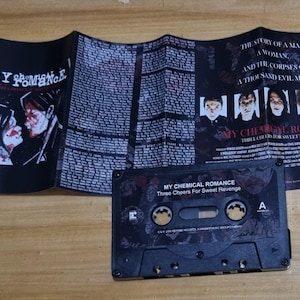 Puede incluir: Una cinta de casete negra con el t&iacute;tulo "My Chemical Romance Three Cheers For Sweet Revenge" impreso en la parte delantera. La cinta de casete est&aacute; en una caja de pl&aacute;stico con una imagen en blanco y negro de una banda en la parte delantera.