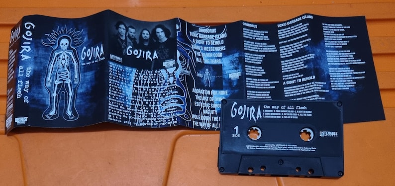 Pu&ograve; includere: Un nastro per cassette nero con il nome della band "GOJIRA" e il titolo dell'album "The way of all flesh" stampato sul lato anteriore. La cassetta &egrave; in una custodia di plastica trasparente con un'etichetta nera.