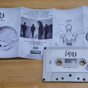 Pu&ograve; includere: Una cassetta audio bianca con il nome della band "Gojira" e il titolo dell'album "From Mars to Sirius" stampati sul lato anteriore. La cassetta audio &egrave; in una custodia di plastica trasparente con un inserto di carta bianca che presenta un'illustrazione in bianco e nero di una balena.