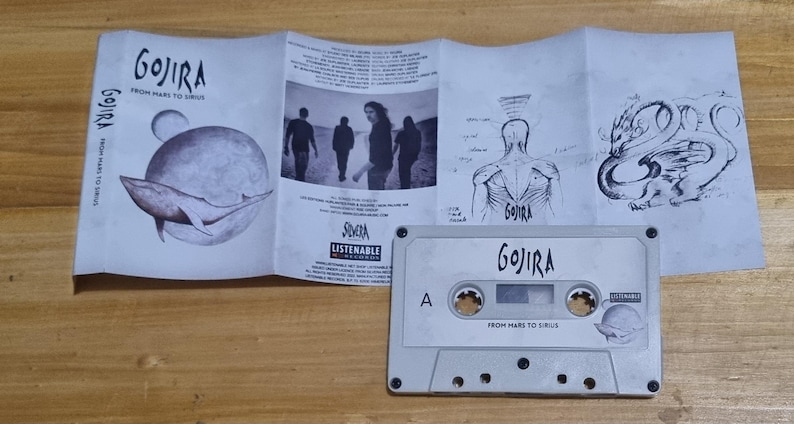 Pu&ograve; includere: Una cassetta audio bianca con il nome della band "Gojira" e il titolo dell'album "From Mars to Sirius" stampati sul lato anteriore. La cassetta audio &egrave; in una custodia di plastica trasparente con un inserto di carta bianca che presenta un'illustrazione in bianco e nero di una balena.