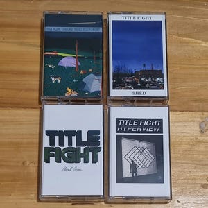 以下が含まれることがあります： 異なるアルバムカバーのついたカセットテープが4つあります。最初のテープは、遠くの建物が見える青い空です。2番目のテープは、テントと焚き火のあるキャンプシーンです。3番目のテープは、幾何学模様の前に立っている人の白黒写真です。4番目のテープは、緑と黒のロゴで、「TITLE FIGHT」という文字と、その下に「Floral Green」という文字が書かれています。