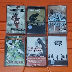 Könnte beinhalten: Sechs Kassetten mit der Band Linkin Park. Die Kassetten sind in verschiedenen Farben und haben unterschiedliche Albumcover. Die Albumtitel sind "Hybrid Theory", "Meteora", "Collision Course", "Reanimation", "Live in Texas" und "Minutes to Midnight".