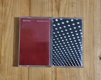 May include: Two cassette tapes. The left tape has a solid red cover with the text "beach house" and "depression cherry". The right tape has a black cover with white polka dots.