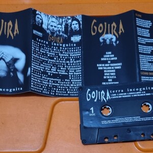 Pu&ograve; includere: Una cassetta audio nera con il nome della band "GOJIRA" e il titolo dell'album "terra incognita" stampati sul lato anteriore. La cassetta audio &egrave; in una custodia di plastica con sfondo nero e testo bianco. La cassetta audio &egrave; etichettata "Lato 1" e ha un adesivo "Listenable" sul lato destro.