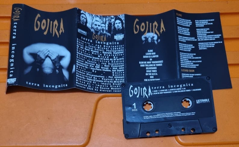 Pu&ograve; includere: Una cassetta audio nera con il nome della band "GOJIRA" e il titolo dell'album "terra incognita" stampati sul lato anteriore. La cassetta audio &egrave; in una custodia di plastica con sfondo nero e testo bianco. La cassetta audio &egrave; etichettata "Lato 1" e ha un adesivo "Listenable" sul lato destro.