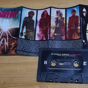 Puede incluir: Una cinta de casete con una caja negra y una etiqueta que dice "My Chemical Romance Danger Days The True Lives of the Fabulous Killjoys".