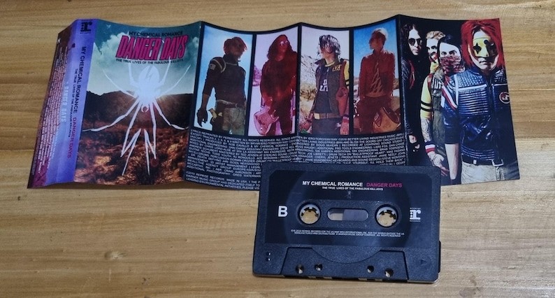 Puede incluir: Una cinta de casete con una caja negra y una etiqueta que dice "My Chemical Romance Danger Days The True Lives of the Fabulous Killjoys".
