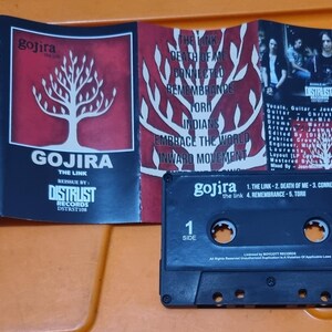 Pu&ograve; includere: Una cassetta audio nera con un'etichetta bianca. L'etichetta riporta il nome della band "Gojira" e il titolo dell'album "The Link". La cassetta &egrave; in una custodia di plastica con una finestra trasparente.