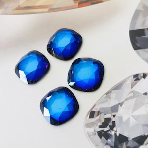 Op de afbeelding: Vier blauwe vierkante strasssteentjes met een facetgeslepen ontwerp.