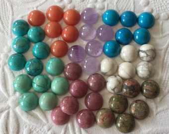 May include: Assortment of cabochon gemstones in various colors, including turquoise, coral, amethyst, and green. The stones are arranged in a circular pattern on a white background.
