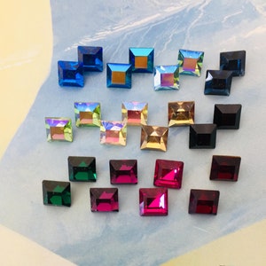 Op de afbeelding: Assortiment van vierkante, iriserende glazen strasssteentjes in verschillende kleuren, waaronder blauw, groen, roze en zwart.