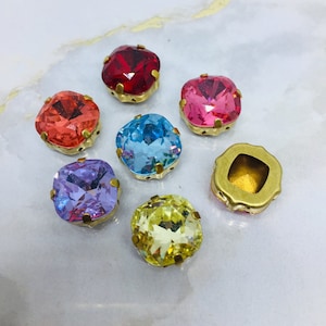 May include: Assortment of colourful square-shaped glass rhinestones with gold settings. The rhinestones are in shades of red, pink, blue, purple, and yellow.