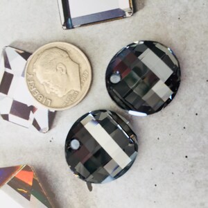 May include: Two black round glass rhinestones with a faceted design. The rhinestones are about 1 inch in diameter.